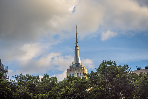 Midtown Manhattan, Manhattan, New York, NY, USA - June 28, 2022: Empire State Building seen against a cloudy afternoon sky above treetops in Bryant Park