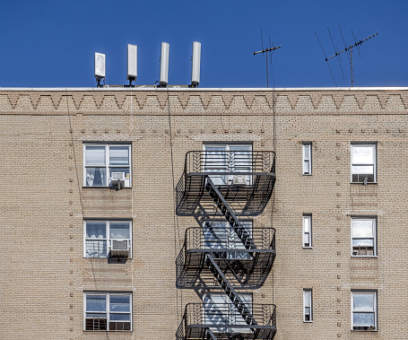 Northern Broadway, Manhattan, New York, NY, USA - June 28, 2022: Façade of a yellow brick building whit fire escape and mobile phone antennas