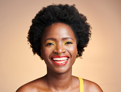 Beautiful, smiling young woman with colorful makeup and cosmetics on her face. Portrait of a happy female enjoying her healthy skin and natural hair. Closeup of an African American lady with a smile