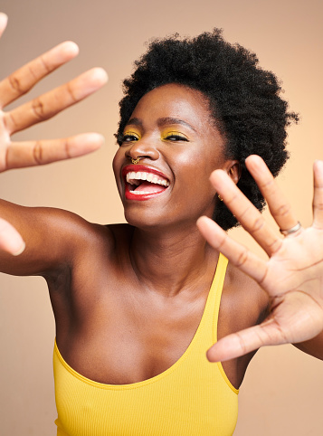 Cheerful, excited and smiling African American woman puts her hands up for the camera. Colorful and bright makeup and clothing on attractive female. Young, funky and happy girl