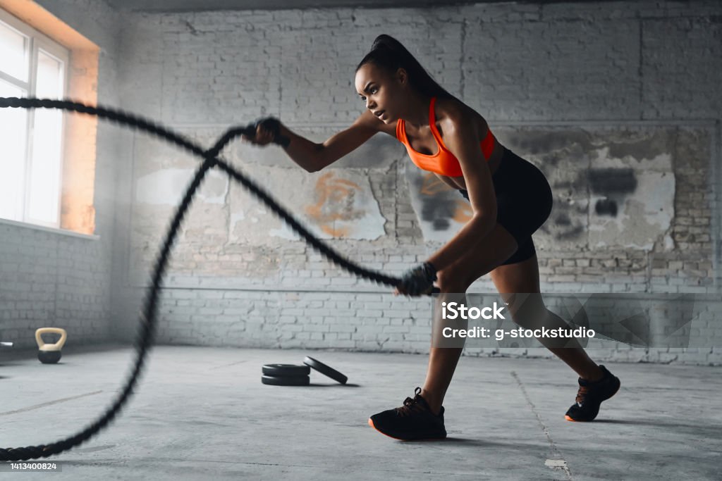 Concentrated young African woman exercising with battle ropes in gym Effort Stock Photo