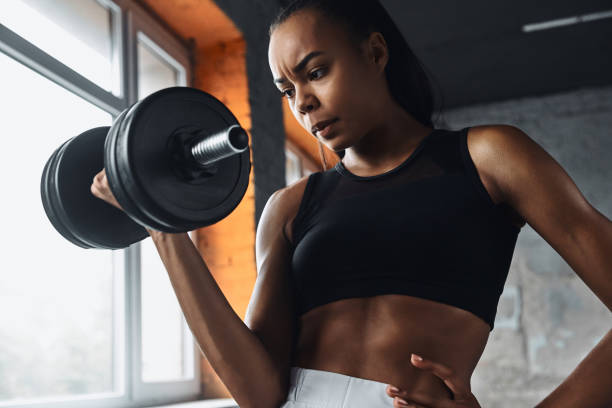 istock Concentrated young African woman using dumbbell while exercising in gym 1413402123