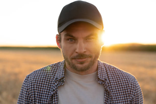 Bearded farmer in a cap and a plaid shirt against the background of a field