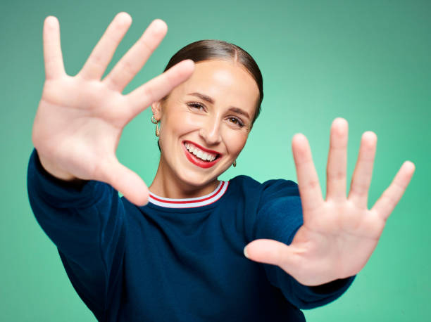 istock Happy woman having fun, looking cheerful and framing her face while posing against a green studio background. Portrait of smiling, carefree and trendy or stylish casual woman showing her hands 1413403352