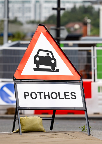Potholes hazard warning sign dangerous road conditions. Red triangle pot hole message warning drivers lack of highway repairs and maintenance.