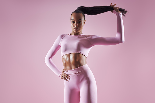 Attractive African woman in sports clothing adjusting her hair against pink background