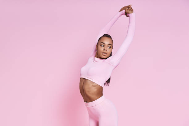 istock Confident young African woman doing stretching exercises against pink background 1413406790