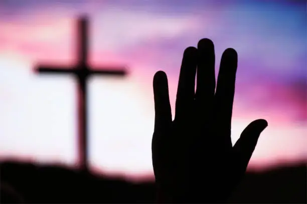 Photo of Hand raising, blurred christian cross background