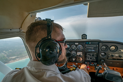 Rear view of a male pilot adjusting switches on the control panel while sitting inside cockpit. Man operating the switches while flying a modern airplane jet.