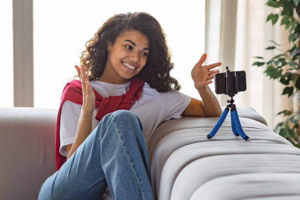 istock Beautiful female content maker uses a mobile phone for online broadcasting. Young attractive African American woman blogger or vlogger looking at camera and talking to followers, technology concept 1413412415