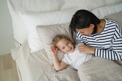 Caucasian young mum having rest with her cute little daughter in bedroom. Woman and kid are happy and falling asleep together. Mother and child are awakening and relaxing at home. Daytime sleep.