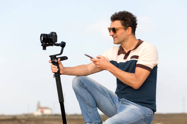 3-axis outdoor vlogger gimbal, smartphone controlled digital camera stabilizer gimbal. Cameraman handle with mobile phone. Phone controlled gimbal cameraman concept in hand. 3-axis mirrorless gimbal gimbal vlogger exterior de 3 ejes, cardán estabilizador de cámara digital controlado por teléfono inteligente. mango de camarógrafo con teléfono móvil. concepto de cámara de cardán controlado por teléfono en la mano. cardán sin espejo de 3 ejes