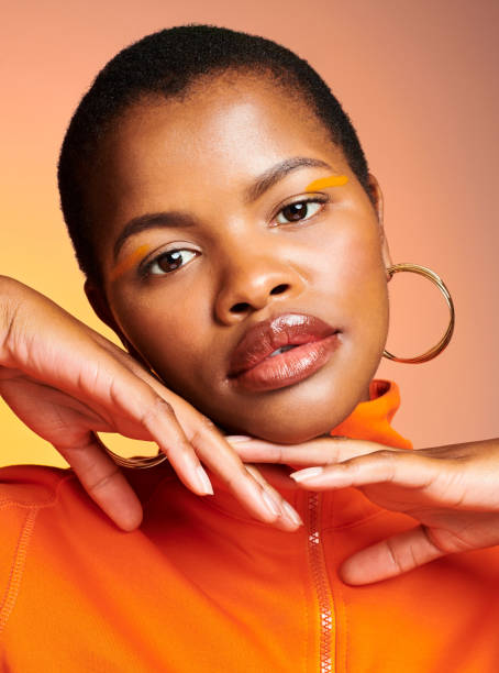 schönes, wunderschönes und attraktives schwarzes weibliches schönheitsmodell mit trendigem make-up im gesicht. porträt einer atemberaubenden afrikanischen stilvollen frau, die ruhig mit kurzen haaren vor leuchtend orangefarbenem hintergrund aussieht - dramatic make up stock-fotos und bilder