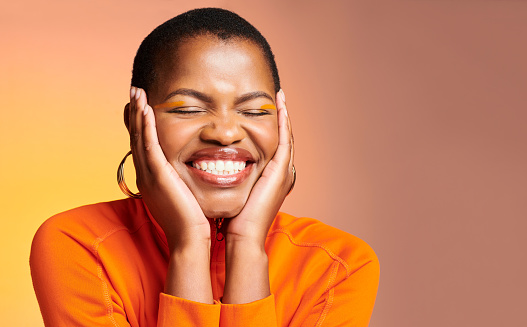 Beauty, colorful and face of beautiful african woman wearing orange makeup and clothing against a studio background with copyspace. Cheerful and edgy female touching her skin and feeling happy
