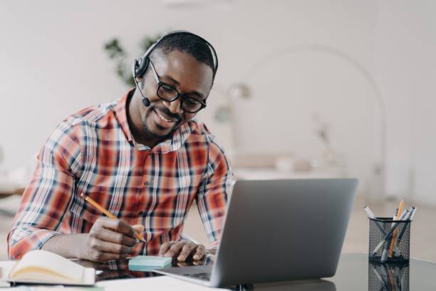 istock African american student in headset learning at laptop online, makes notes. Distance education 1413417677