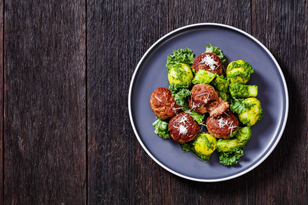 Lihapullat, beef meatballs and boiled new potatoes coated with basil pesto on plate on dark wooden table, horizontal view from above, flat lay, free space