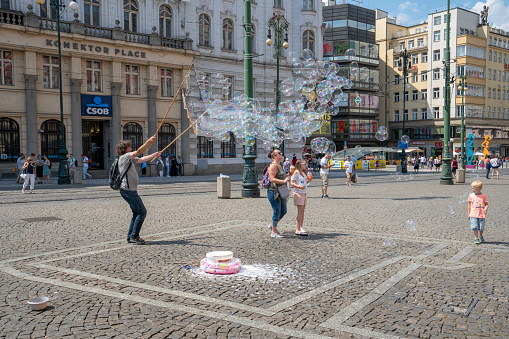 Prague - April 25, 2017:  Street performer making bubbles to entertain people. People are walking around in center and watching a show.
