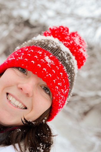 Happy smiling young woman wearing a woolly red bobble hat with snowflakes on it in Lapland, happy to be meeting Santa in a few day.
