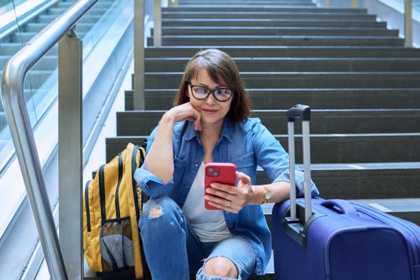 Woman passenger with suitcase backpack sitting on steps in modern building stock photo