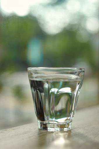 Glass plenty of water on wooden table next to window.