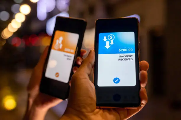 Cropped image of a man and a woman's hand holding smartphone, sending money through digital wallet. Smart banking with technology.