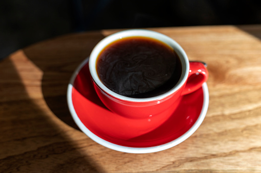 Red coffee cup on wooden table against morning sun light