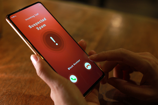 A woman receiving an incoming suspected spam call on her phone. The network provider detect the scam and show warning sign, woman rejects the call.