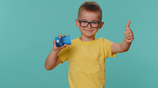 Toddler children boy kid showing plastic credit bank card advertising transferring money cashless, purchases online shopping, sale discount, internet order delivery purchase on blue studio background