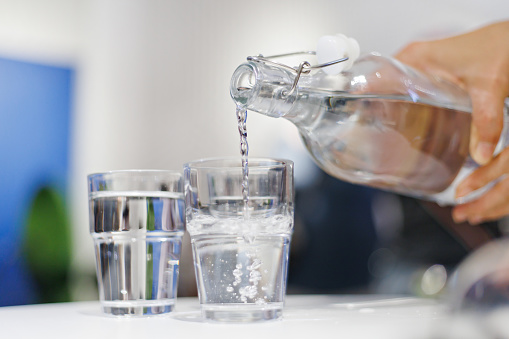 Cropped image of woman pouring water from bottle into the glass in a restaurant. Healthy lifestyle and stay hydrated