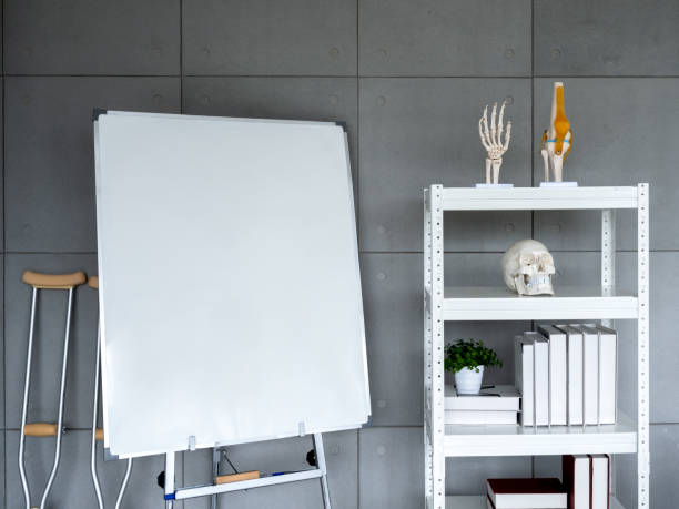 istock Orthopedic doctor office background decoration with empty blank white board, crutches, skull, wrist and knee bone model on bookshelf on grey background. Interior of modern doctor's office in clinic. 1413438704