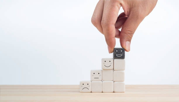 istock Feedback, client survey, customer experience satisfaction rating scale with emoticon face. Hand put the happy smile face on black cube on the top of white cube blocks on the growth chart steps. 1413438748