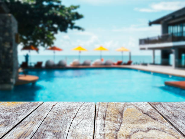istock Close-up empty space on old wooden plank table or deck floor in front of the blurred pool, beach and open sky background on sunny day. Empty space for product at poolside, summer background. 1413438833