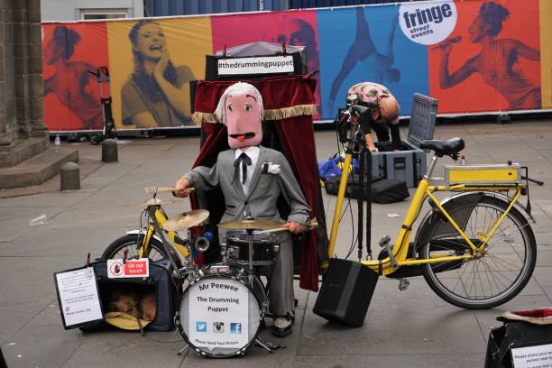 Edinburgh, Scotland - 6 August 2022: A street performer (Puppeteer / Drummer) is performing on the Royal Mile during the Edinburgh Fringe, the first year of post-pandemic activity. In the background a previous act is packing up.