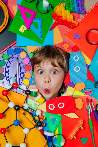 Funny girl's face surrounded by different school stationery. Top view, flat lay. Back to school concept background.