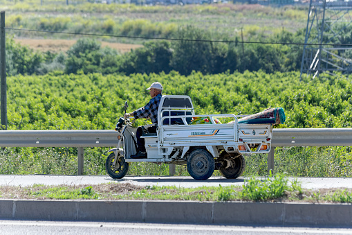 Canakkale, Turkey - Jun 09 2021: Old man carry carpet with three wheel electric pickup truck on the highway.