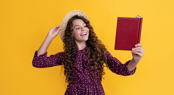 cheerful child with frizz hair recite book on yellow background.