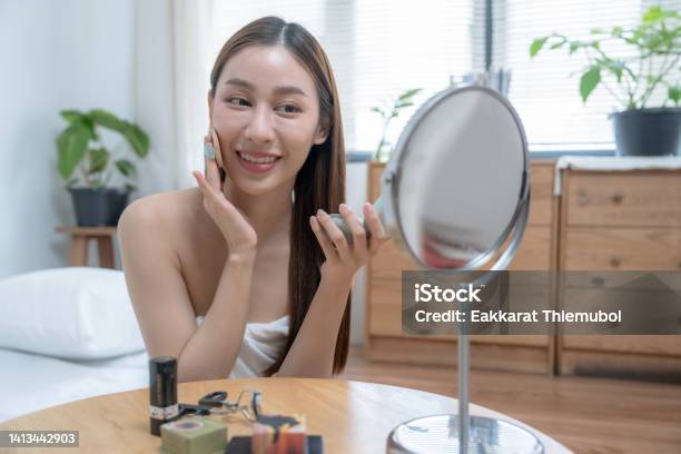 自宅の寝室で化粧をしている美しい若いアジア人女性。
