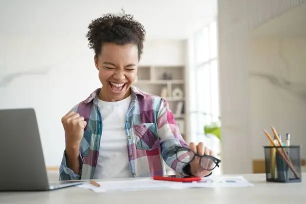 Photo of Excited biracial girl student celebrates victory, got email with good scores. Personal achievement