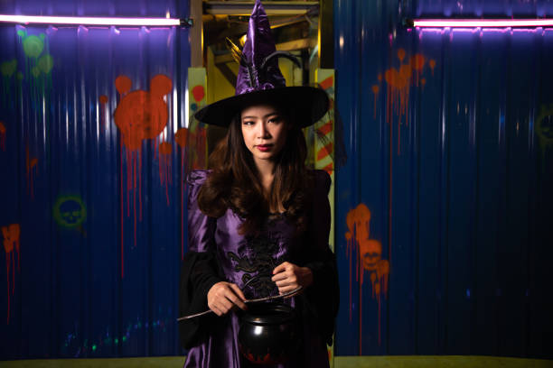 Beautiful young woman in witches hat and costume. Halloween witch with magic lights in a dark night. Halloween party.