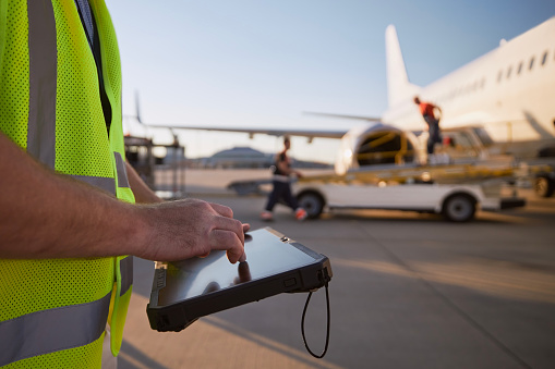 Member of ground crew preparing airplane before flight. Worker using tablet against plane at airport.