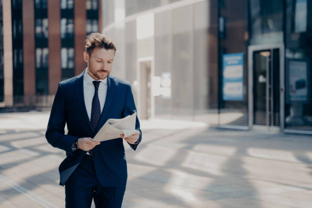 istock Successful businessman in formal wear reads newspaper while walking 1413446952