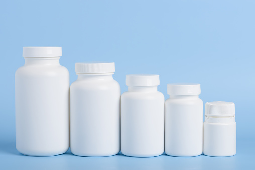 Blank white plastic bottles of medicine pills or supplements in a row on blue background