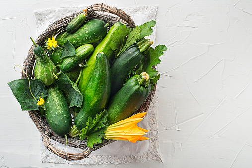 Basket of fresh vegetable crops with zucchini and cucumber on white background