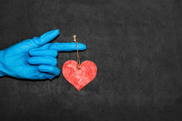 hand in medical gloves holds a small heart on black background stock photo
