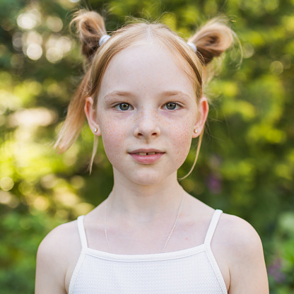 Portrait of redhead girl with freckles on summer blurred background. Cheerful and happy childhood