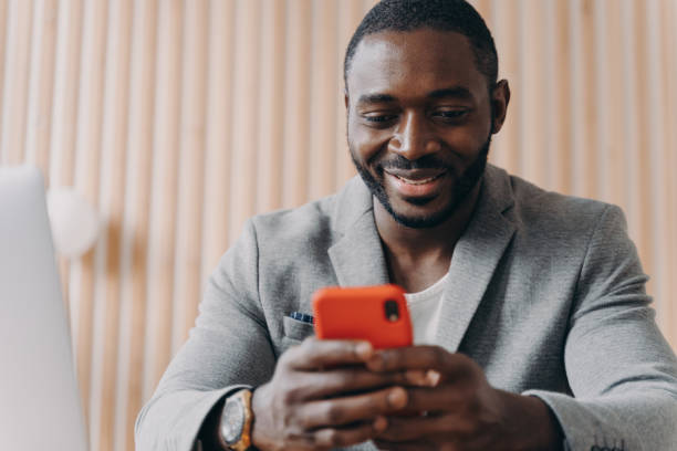 istock Cheerful young afro american man chatting online on smartphone looking on phone screen with smile 1413449614