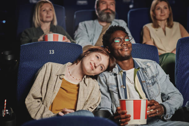 Lovely Couple At Cinema Portrait of modern lovey-dovey ethnically diverse young couple spending evening on date at cinema cinema stock pictures, royalty-free photos & images