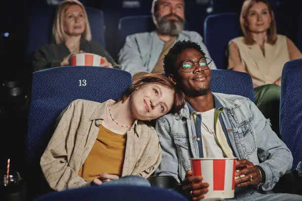 Portrait of modern lovey-dovey ethnically diverse young couple spending evening on date at cinema