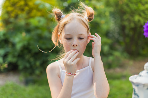 Portrait of redhead girl with freckles on summer blurred background. Cheerful and happy childhood. Girl eating a baguette outdoors. Summer picnic vacation. Outdoor recreation. Leisure activity
