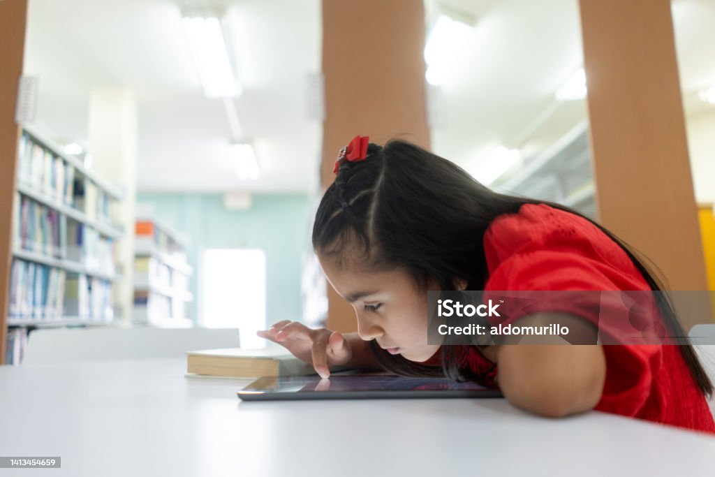 Shortsighted little girl using tablet with face close to screen A shortsighted little latin girl using a digital tablet with her face close to the screen. Child Stock Photo